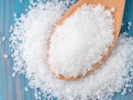 large wooden spoon with big sea salt for the bright blue wooden background, on the table scattered salt crystals, top view