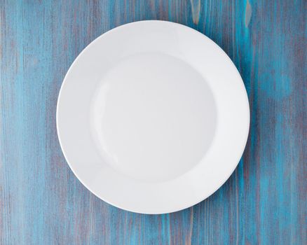 big flat empty white plate on a blue wooden table, top view