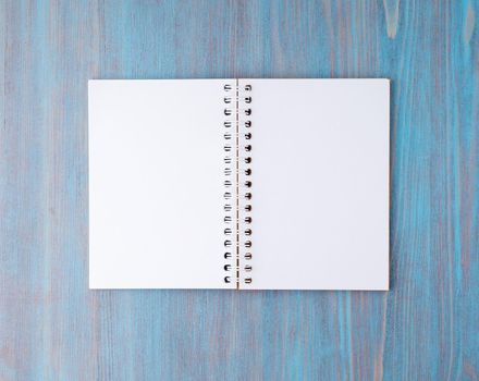 Open notebook on spring with white paper for notes and drawing. Light background, blue wood, top view.