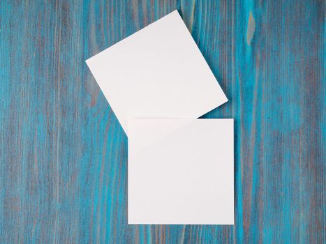 two white piece of paper for notes, square shape for record reminders on a blue wooden table, top view
