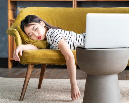 Young Asian girl fell asleep oncouch in front oflaptop. Cute bored woman watching boring movie, sad Sunday, dull leisure tired or overworked. Cozy home environment, soft sofa