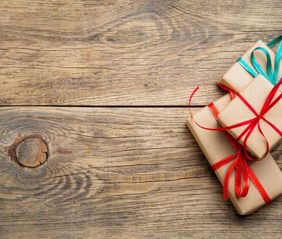 Three gift boxes of Kraft paper with ribbons on a brown wooden background, top view, copy space. Shopping, Valentines day