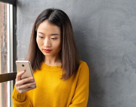 Serious, thoughtful beautiful young Asian woman looking at mobile phone, reading messages, browsing information on Internet. Pretty female using cellphone and making selfie