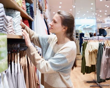 Women chooses clothes in large offline store, touches different things on shelves. Concept of visiting mass events and public places where coronavirus is easily transmitted