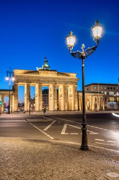 The backside of the illuminated Brandenburg Gate in Berlin with a historic street light at dawn