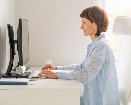 Nice beautiful female working on pc sitting at home. Online shoping, alternative office freelance, gig economy, digital nomad. Side view of middle aged woman working remotely from home