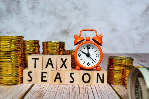 Tax text on wooden blocks and alarm clock set at 10 o'clock on table with gold coins and dollar background. Business and tax concept.