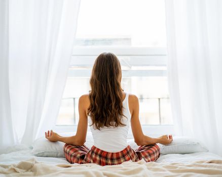 Back view of woman yoga pose in bed after wake up, entering new day happy and relaxing after good night sleep. Sweet dreams, good morning, weekend, holidays concept