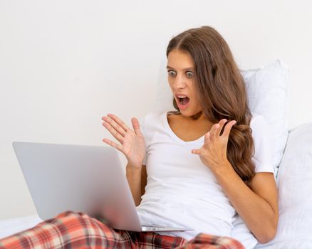 Female angering and annoying, broken Internet line. Young woman student watch video online webinar learn on laptop, siting in bed distance elearning course bedroom at home. Avoiding social contact.