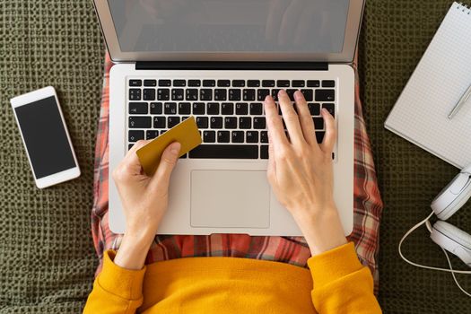 Online shopping concept. Unrecognizable woman sitting at bed, paying for purchases by credit card, planning travel, choosing vacation, looking for tickets, booking hotel