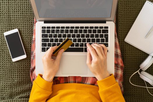 Online shopping concept. Unrecognizable woman sitting at bed, paying for purchases by credit card, planning travel, choosing vacation, looking for tickets, booking hotel