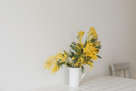 Spring flowers composition. Yellow mimosa flowers on white background in home interior.