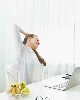 Woman stretches her arms, kneads her back from fatigue. Long sitting at computer, muscle cramps. Distance learning for students. Quarantine, self-isolation, social phobia. E-learning