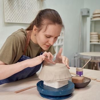 Concentrated young woman ceramist working on clay ware with satisfaction as recreation in creative art studio