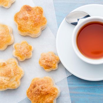 traditional breakfast with a cup of tea and sweet pastries - scones, a mug of tea, spoon, on wooden blue table, top view.