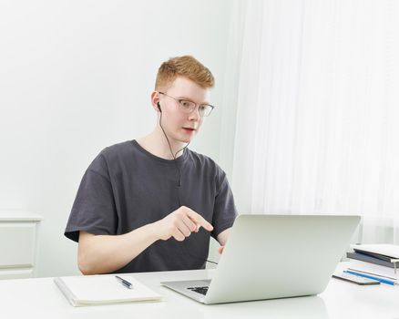 Distance learning or working. Quarantine, self-isolation, social phobia. Young boy speaking on online training, meeting, conference. Man looks at laptop. Freelancer, Concept Of Digital Nomad