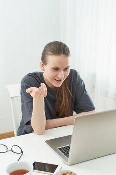 Girl listens or looks at information on computer with disbelief. Skeptical expression on his face. Fake news. Distance education for students. Quarantine, self-isolation, sociophobia.