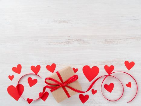 symbol of Valentine's day - gift box in kraft brown paper with red ribbon on pink background with lots of red hearts, top view, copy space for text