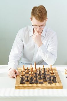 Quarantine, self-isolation. Home games, Hobbies. Smart red-haired guy with glasses one is playing chess with himself, thinking about next move, rubbing his chin