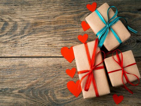 Valentine's day background. Gifts wrapped with Kraft brown paper, with red ribbons, hearts on aged rustic vintage old wooden background