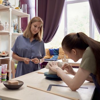 Side view of pottery master teaching young student modeling clay bowl as art recreation in creative handwork studio