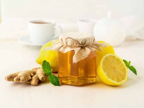 Popular ways to treat a cold - a jar of honey, ginger, mint, lemons on white background, side view