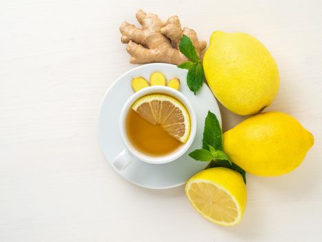 Folk ways to treat colds - cup of tea and a slice of lemon, ginger, mint, whole lemons and half on a white background, top view.