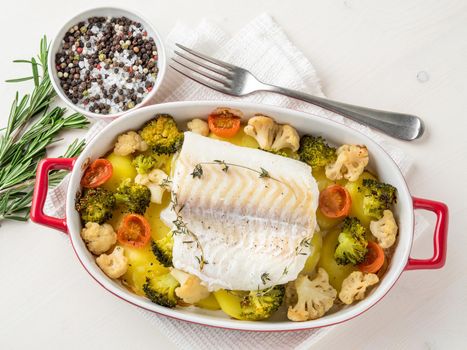 Fish cod baked in the oven with vegetables - healthy diet healthy food. Light white wooden background, top view.