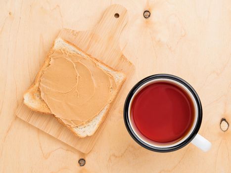 toast with peanut butter, spreading on sandwich, mug of tea on a beige wood background