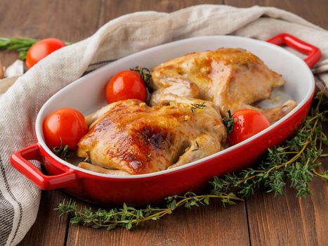 two carcasses fried chicken in a bowl, baked chucks in an oven with tomatoes, with crispy crust on dark brown wooden rustic table, side view