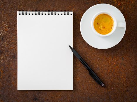 white empty blank sheet of notebook with a spiral, pencil and cup of coffee on rusted old iron table, top view.