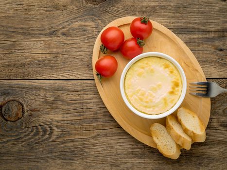 wood plate with oven-baked omelet of eggs and milk, with tomatoes and toast on brown rustic wooden table, top view, copy space