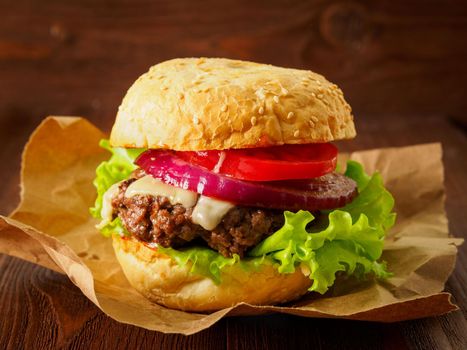 Big delicious homemade burger with beef cutlet, cheese, onion, tomato and lettuce on toasted rolls. American fast food, unhealthy eating. Side view, selective focus