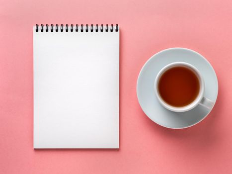 Blank notepad white page and cup of tea on pink desk, color background. Top view, flat lay.