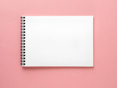 Blank notepad white page on pink desk, color background. Top view, flat lay.