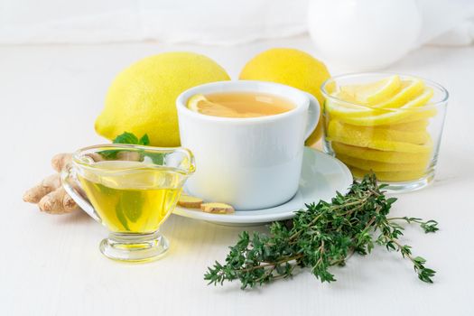 Folk popular ways to treat colds - cup of tea and a slice of lemon, ginger, mint, honey, herbs, whole lemons and half on a white background, side view.