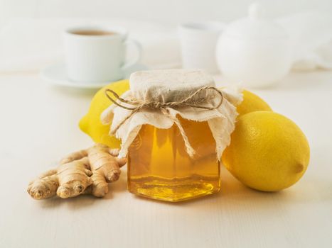 Popular ways to treat a cold - a jar of honey, ginger, lemons on white background, side view