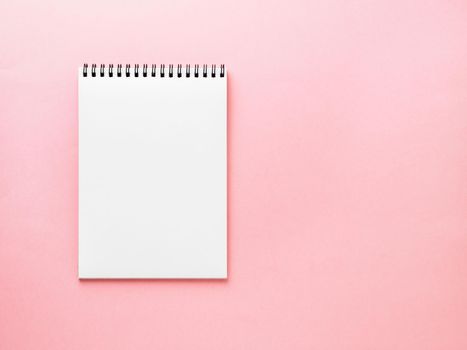 Blank notepad white page on pink desk, color background. Top view, empty space for text.