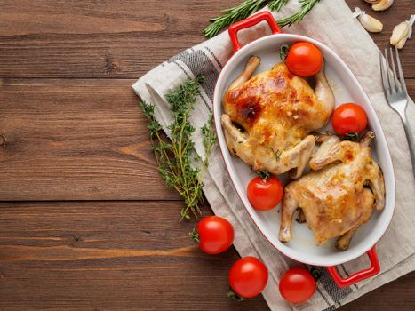 two carcasses fried chicken in a bowl, baked chucks in an oven with tomatoes, with crispy crust, on dark brown wooden rustic table, top view, copy space for text