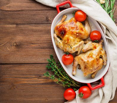 two carcasses fried chicken in a bowl, baked chucks in an oven with tomatoes, with crispy crust, on dark brown wooden rustic table, top view, copy space for text