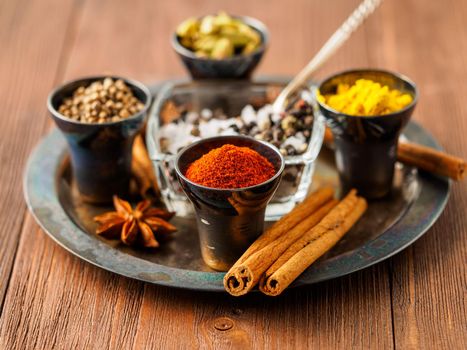 Oriental spice set - coriander, red pepper, turmeric, cinnamon, star anise, rosemary various seasonings in metall cups, on brown wooden table, side view, mcro, selective focus.