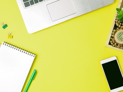 Top view of modern bright yellow office desktop with blank notepad, computer, smartphone. Mock up, empty space