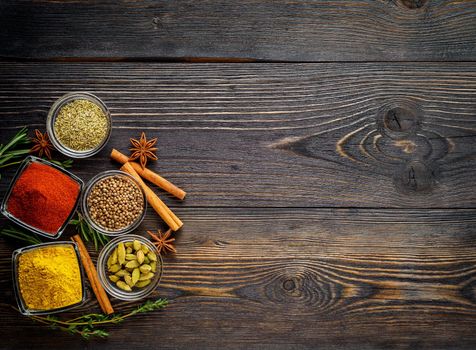 Set of spices and herbs on dark brown textured wooden table. Top view, empty space