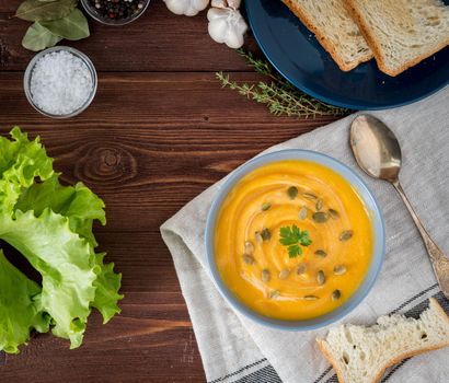 Dietary vegetarian pupmkin cream soup puree, on dark brown wooden table, top view, close up.