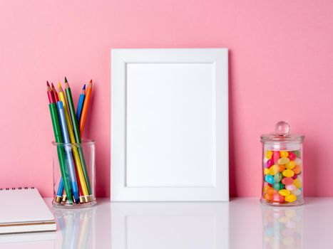 Blank white frame and crayon in jar, candys on a white table against the pink wall with copy space