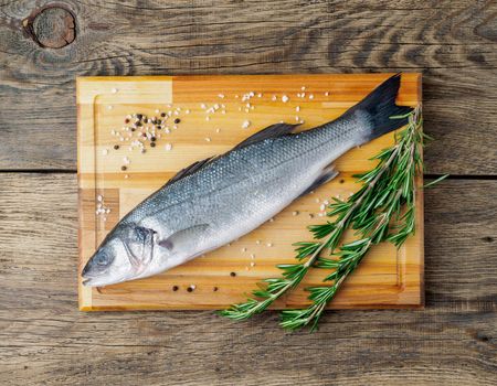 fresh, raw, saltwater fish, sea bass on a wooden cutting board on old wooden aged, rustic table, top view