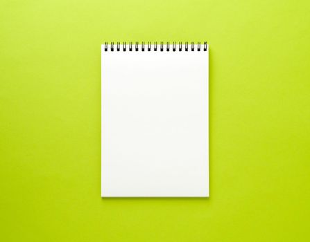 Blank notepad white page on green desk, color background. Top view, empty space for text.