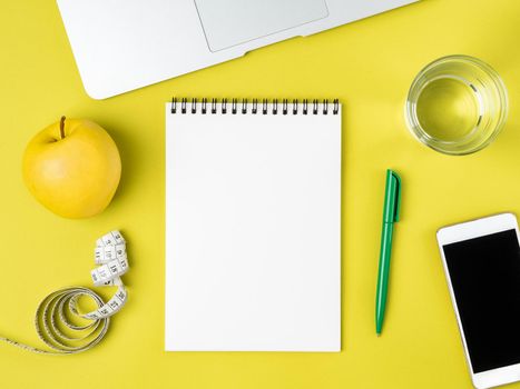 Blank Notebook page for Diet plan or menu, tape measure, water in glass and apple on bright yellow background, weight loss concept, top view.