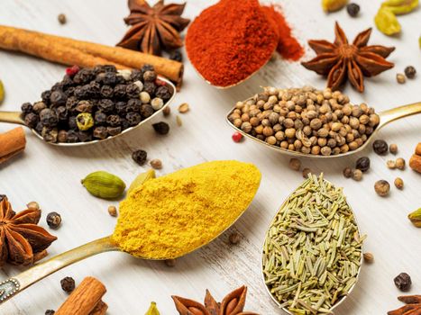 Mix of Indian spices in spoons on white wooden table, side view, selective focus, macro. Seasonings - rosemary, curry, pepper, paprika.