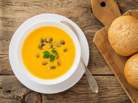 white bowl of pumpkin soup, garnished with parsley and sunflower seeds on wooden background